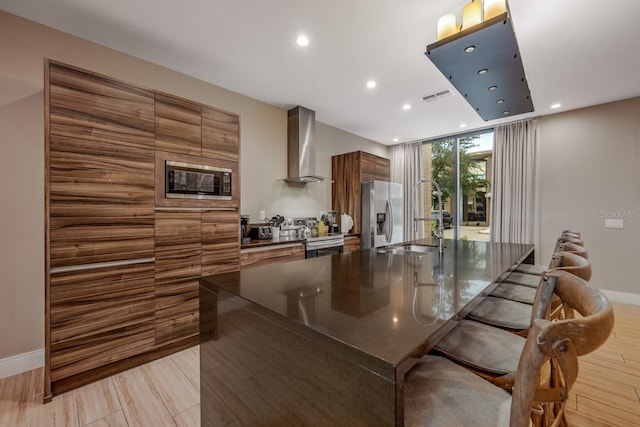 kitchen with sink, wall chimney exhaust hood, a kitchen bar, a kitchen island with sink, and appliances with stainless steel finishes