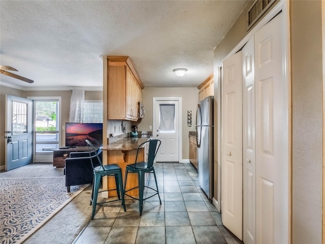 kitchen featuring light brown cabinets, ceiling fan, kitchen peninsula, a breakfast bar area, and stainless steel refrigerator