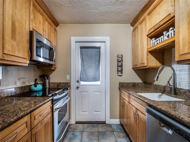 kitchen featuring a textured ceiling, sink, appliances with stainless steel finishes, and dark stone counters