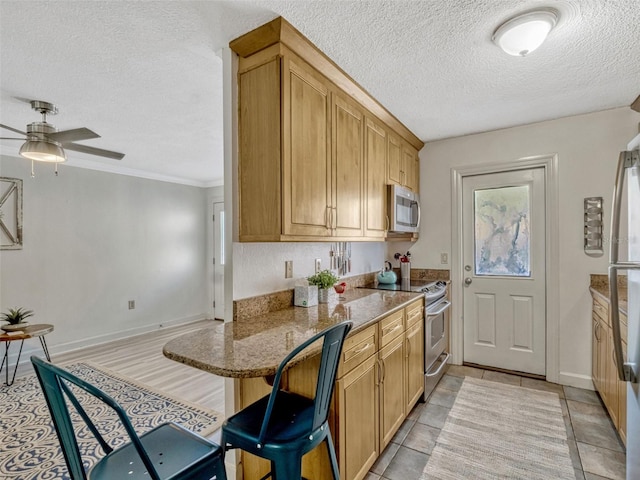 kitchen featuring a kitchen breakfast bar, stainless steel appliances, dark stone countertops, a ceiling fan, and a textured ceiling