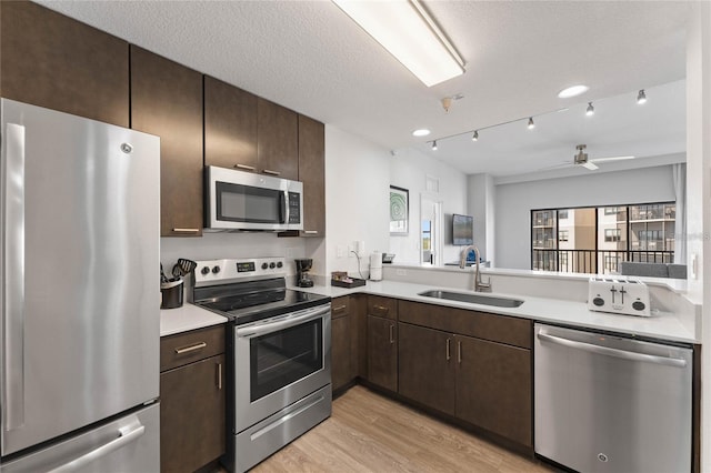 kitchen with appliances with stainless steel finishes, a textured ceiling, ceiling fan, sink, and light hardwood / wood-style flooring