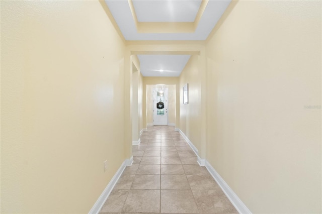 hallway featuring a tray ceiling and light tile patterned flooring