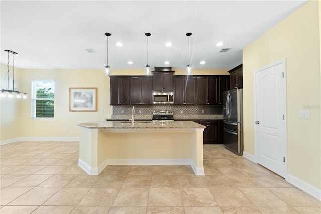 kitchen with light stone countertops, a kitchen island with sink, stainless steel appliances, decorative light fixtures, and decorative backsplash