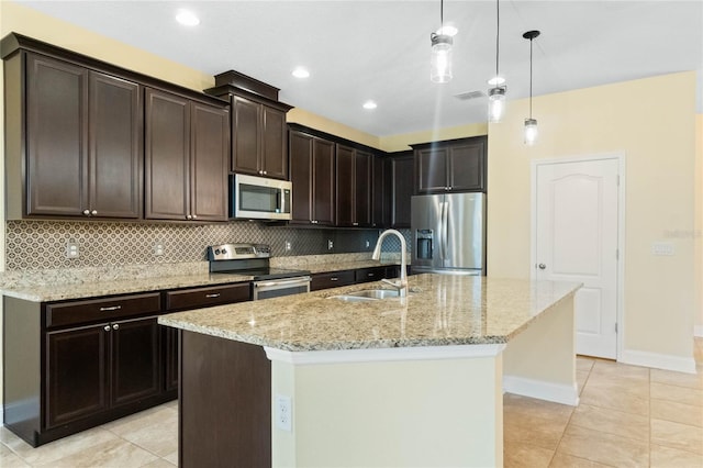 kitchen featuring a center island with sink, sink, appliances with stainless steel finishes, tasteful backsplash, and decorative light fixtures