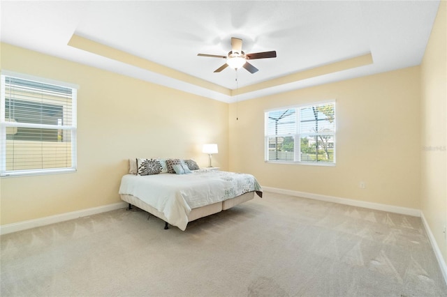 carpeted bedroom featuring a tray ceiling and ceiling fan