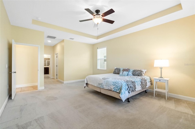 bedroom with ceiling fan, light carpet, and a tray ceiling