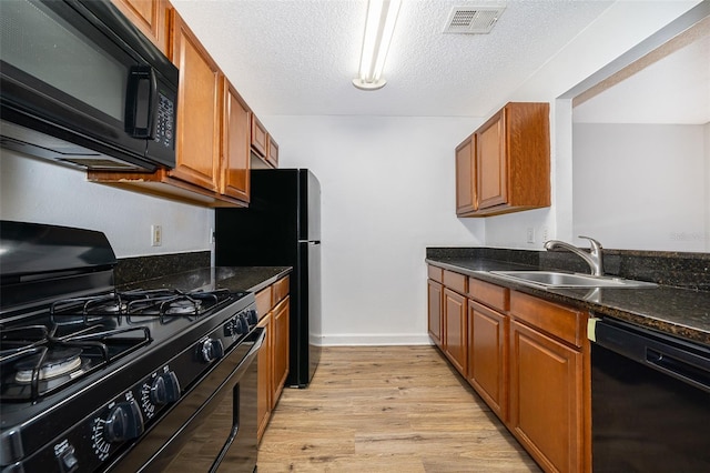 kitchen featuring black appliances, sink, dark stone countertops, a textured ceiling, and light hardwood / wood-style floors