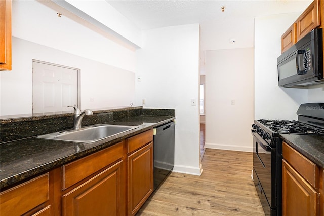 kitchen with black appliances, light wood-type flooring, sink, and dark stone counters