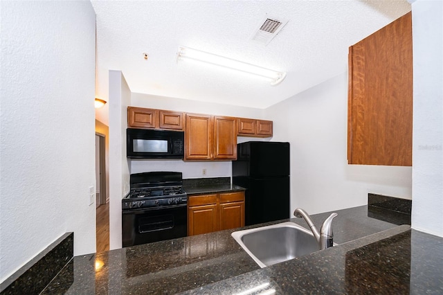 kitchen featuring dark stone counters, sink, black appliances, and a textured ceiling