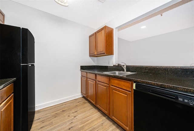 kitchen featuring dark stone countertops, sink, black appliances, and light wood-type flooring