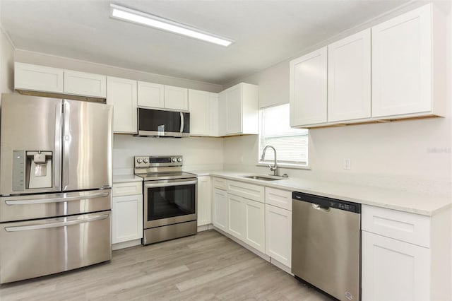 kitchen with light wood finished floors, stainless steel appliances, light countertops, white cabinets, and a sink