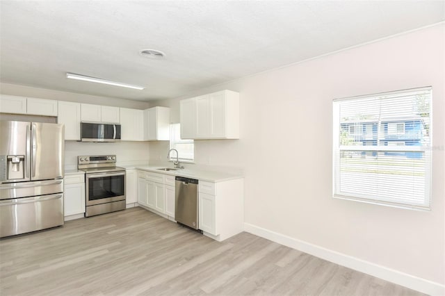 kitchen with stainless steel appliances, light countertops, white cabinets, a sink, and light wood-type flooring