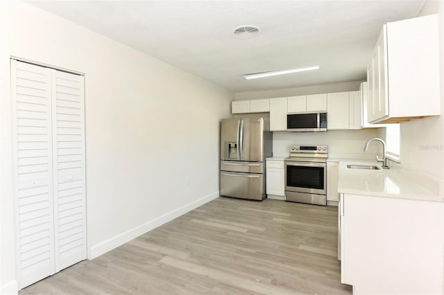 kitchen with stainless steel appliances, light countertops, light wood-style floors, white cabinetry, and a sink