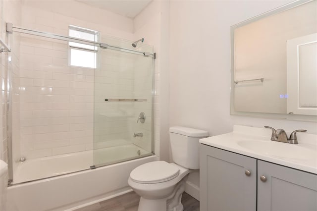 bathroom with vanity, shower / bath combination with glass door, wood finished floors, and toilet