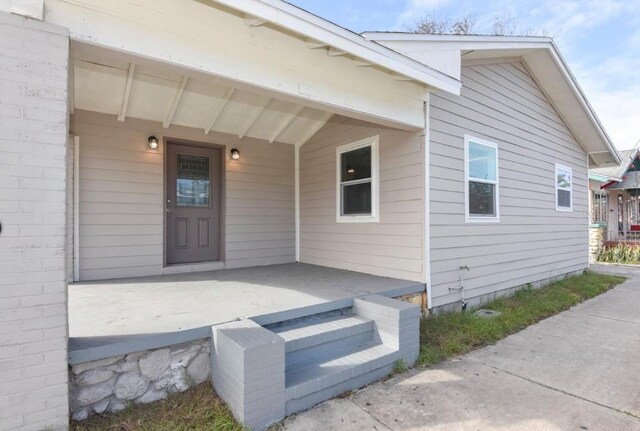 view of exterior entry with a porch and brick siding