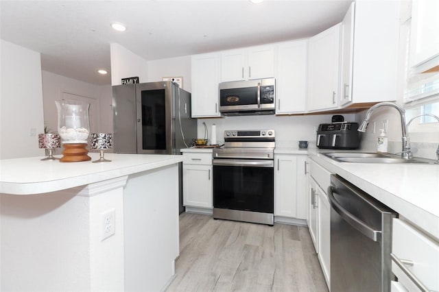 kitchen with appliances with stainless steel finishes, light hardwood / wood-style flooring, white cabinetry, and sink