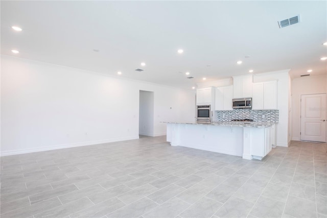 kitchen featuring light stone countertops, a kitchen island with sink, decorative backsplash, white cabinets, and appliances with stainless steel finishes