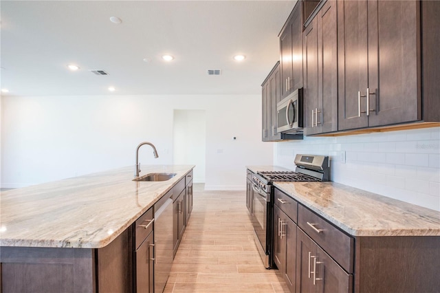 kitchen with light stone countertops, appliances with stainless steel finishes, a kitchen island with sink, sink, and light hardwood / wood-style floors