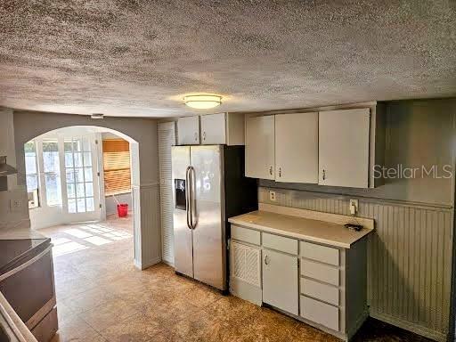 kitchen with arched walkways, light floors, stainless steel appliances, light countertops, and wainscoting