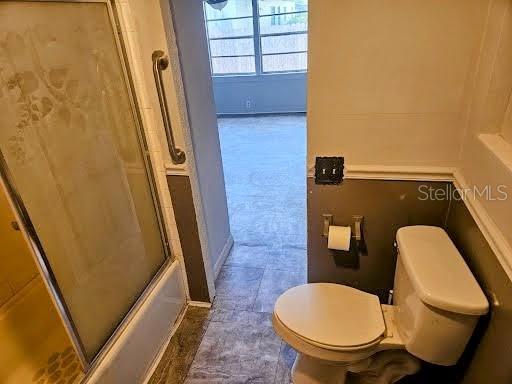 full bathroom with toilet, enclosed tub / shower combo, and baseboards