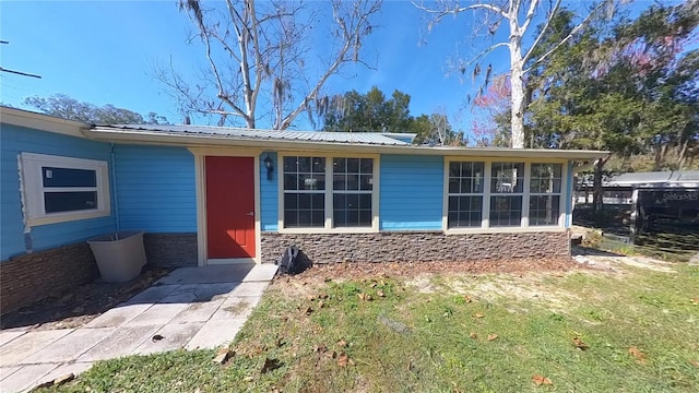 exterior space featuring stone siding, metal roof, and a front lawn