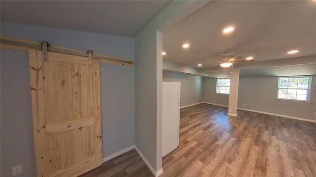 basement with recessed lighting, a barn door, ceiling fan, wood finished floors, and baseboards