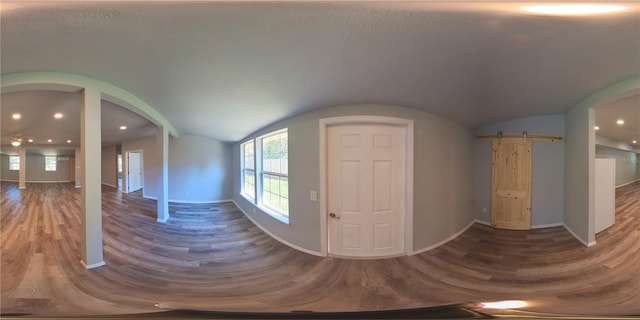 entrance foyer featuring a barn door, vaulted ceiling, baseboards, and wood finished floors