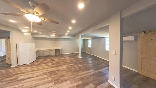 basement featuring hardwood / wood-style floors, ceiling fan, white refrigerator, and an AC wall unit