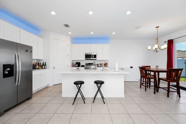 kitchen featuring white cabinets, decorative light fixtures, stainless steel appliances, and an island with sink