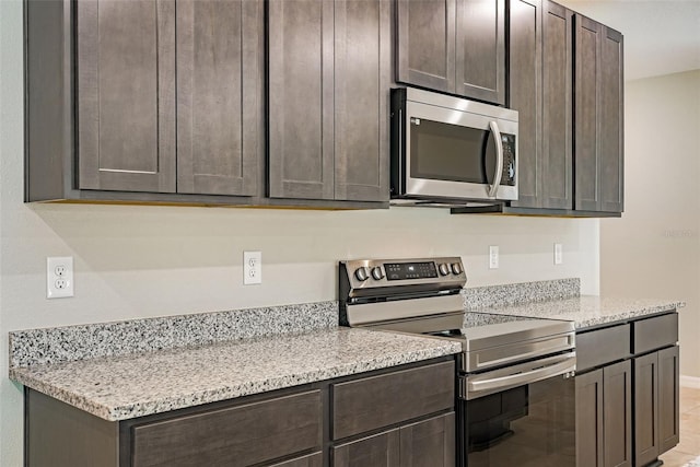 kitchen with dark brown cabinets, light tile patterned floors, light stone countertops, and appliances with stainless steel finishes