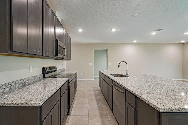 kitchen featuring stainless steel appliances, light stone counters, a kitchen island with sink, and sink