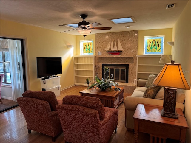 living room featuring a skylight, hardwood / wood-style flooring, ceiling fan, and a premium fireplace