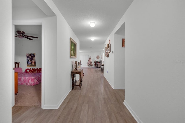 hallway with a textured ceiling and light hardwood / wood-style flooring