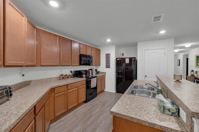 kitchen with sink, a center island with sink, light hardwood / wood-style floors, and black appliances