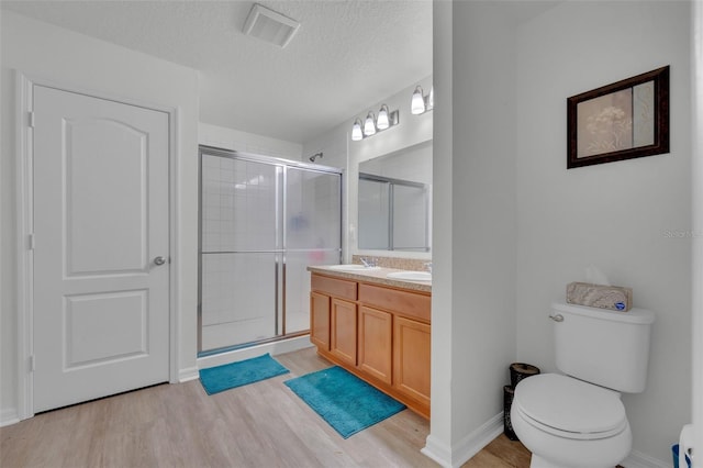 bathroom featuring an enclosed shower, vanity, a textured ceiling, hardwood / wood-style flooring, and toilet