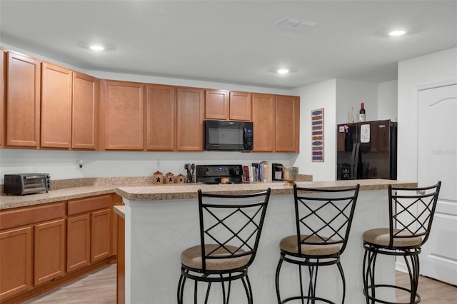 kitchen featuring black appliances, a center island, a kitchen bar, and light hardwood / wood-style flooring