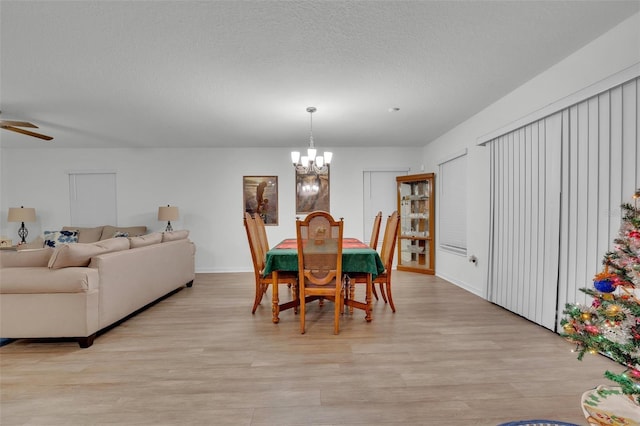 dining space featuring ceiling fan with notable chandelier, a textured ceiling, and light wood-type flooring