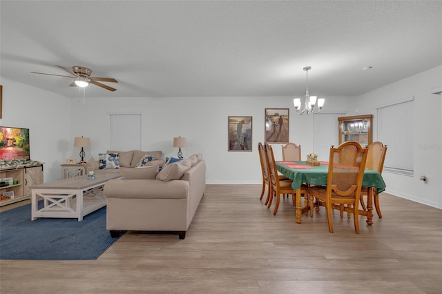 dining space featuring ceiling fan with notable chandelier, a textured ceiling, and light hardwood / wood-style flooring