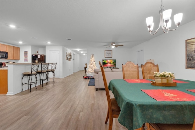 dining space featuring ceiling fan with notable chandelier and light hardwood / wood-style floors