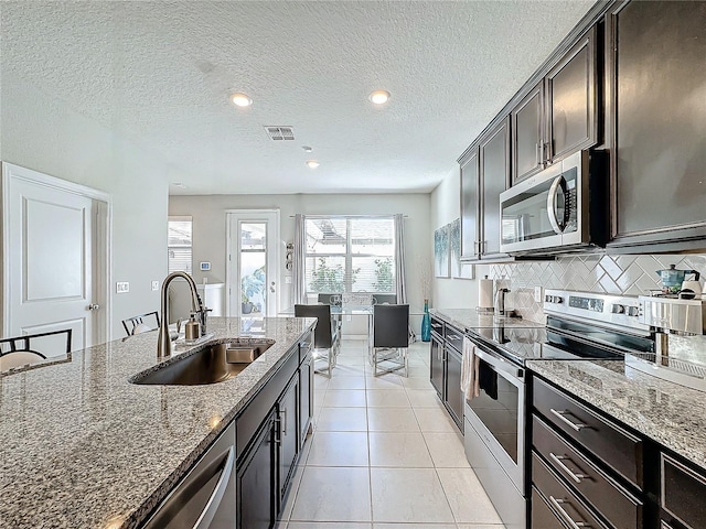 kitchen with sink, dark stone countertops, light tile patterned floors, tasteful backsplash, and stainless steel appliances