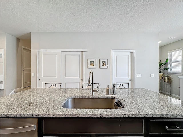 kitchen with a kitchen island with sink, sink, light stone countertops, and a textured ceiling