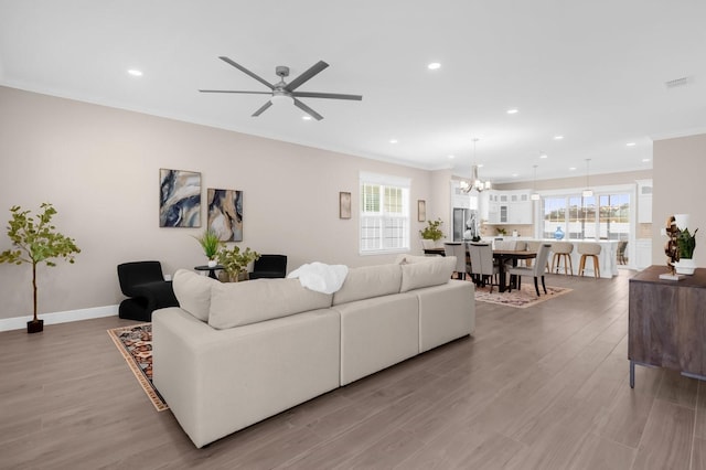 living room featuring a wealth of natural light, hardwood / wood-style floors, crown molding, and ceiling fan with notable chandelier