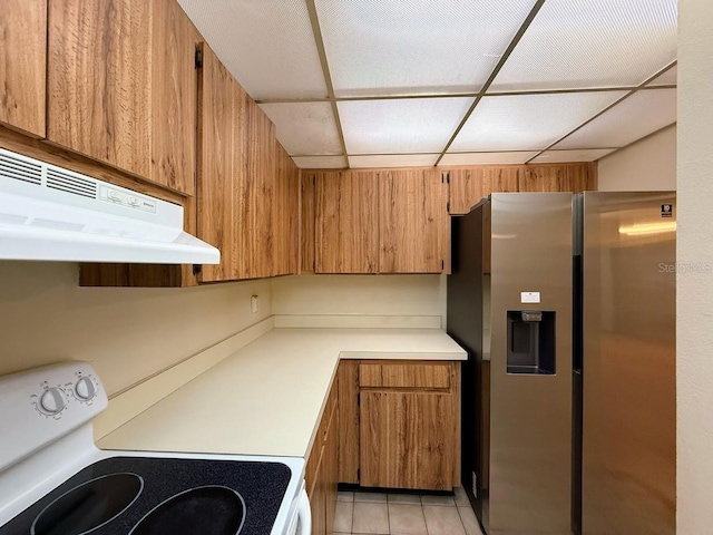 kitchen featuring a drop ceiling, stainless steel fridge, stove, extractor fan, and light tile patterned flooring