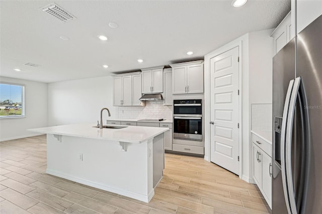 kitchen with appliances with stainless steel finishes, white cabinetry, sink, a kitchen breakfast bar, and a center island with sink