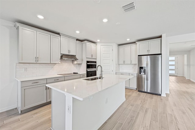 kitchen with sink, light wood-type flooring, black appliances, and an island with sink