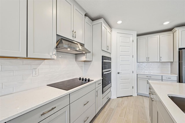 kitchen featuring light stone counters, light hardwood / wood-style floors, backsplash, and appliances with stainless steel finishes