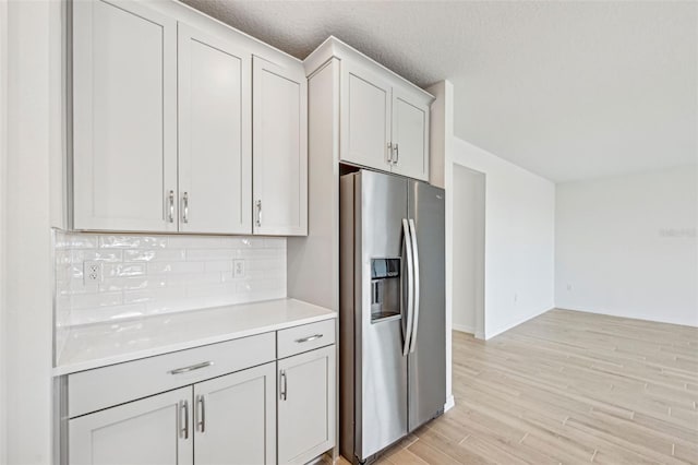 kitchen featuring stainless steel fridge with ice dispenser, white cabinetry, light hardwood / wood-style floors, decorative backsplash, and a textured ceiling