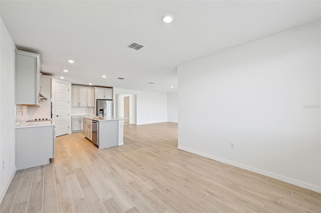 kitchen with stainless steel appliances, decorative backsplash, light hardwood / wood-style floors, and an island with sink