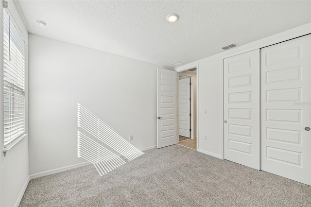 unfurnished bedroom featuring light carpet, a closet, and a textured ceiling