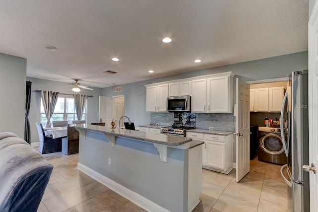 kitchen featuring a kitchen bar, appliances with stainless steel finishes, light stone counters, white cabinetry, and an island with sink